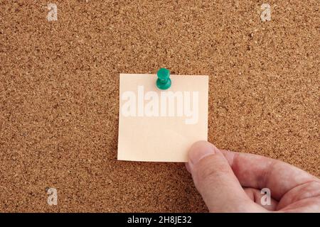 Ein Mann mit einer leeren Haftnotiz, die an einem Korkbrett befestigt ist. Nahaufnahme. Stockfoto