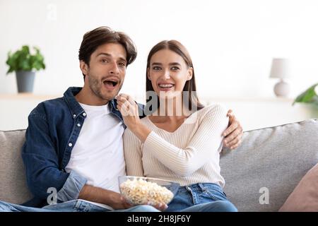 Lächelnd fröhlich überrascht glückliches junges europäisches Paar, das Popcorn isst und sich einen lustigen Film ansieht Stockfoto