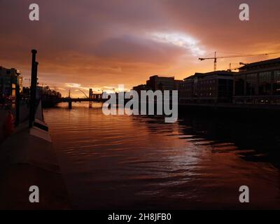 DUBLIN, IRLAND - 04. Dez 2019: Die Silhouetten von Gebäuden und ein orangefarbener Himmel bei Sonnenaufgang über dem Liffey in Dublin. Blick in Richtung Hafen von Dublin. Stockfoto