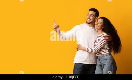 Schönes Angebot. Glückliche Junge Arabische Ehegatten Zeigen Beiseite Auf Copy Space Stockfoto