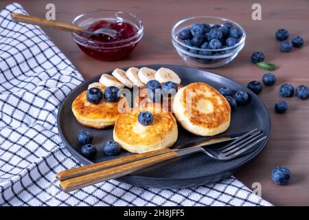 Hüttenkäse-Pfannkuchen, Pfannkuchen mit Quark, Syrniki mit frischen Beeren und Banane, Marmelade, Sauerrahm zum Frühstück. Selektiver Fokus. Stockfoto