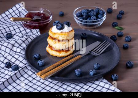 Quark-Pfannkuchen, Quark-Pfannkuchen, Syrniki mit frischen Beeren, Marmelade, Sauerrahm zum Frühstück. Selektiver Fokus. Stockfoto