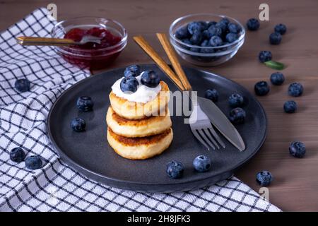 Quark-Pfannkuchen, Quark-Pfannkuchen, Syrniki mit frischen Beeren, Marmelade, Sauerrahm zum Frühstück. Selektiver Fokus. Stockfoto