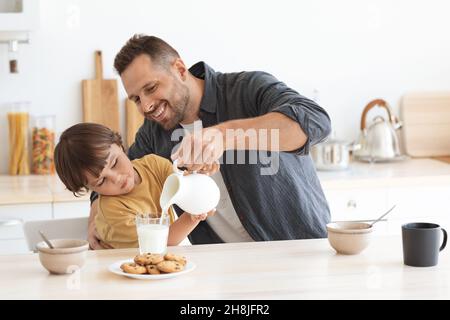 Lieblingsgetränk am Morgen. Glücklicher kleiner Junge, der seinem Vater dabei hilft, Milch in Glas zu gießen und zu Hause ein gesundes Frühstück zu genießen Stockfoto