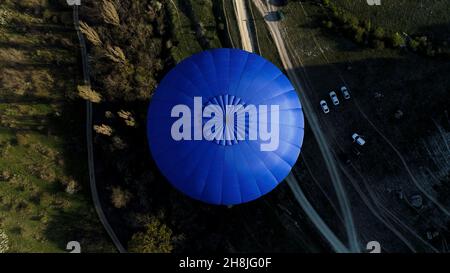 Luftaufnahme eines blauen Ballons am Himmel über der Landschaft, Frankreich. Aufnahme. Fliegen über Bäumen, Büschen, grünen Feldern und Parkautos Stockfoto