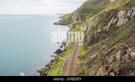 Ein DART-Zug steigt aus einem Tunnel auf der Küstenbahnlinie an den Klippen zwischen Bray und Greystones in der Grafschaft Wicklow, Irland, aus. Stockfoto