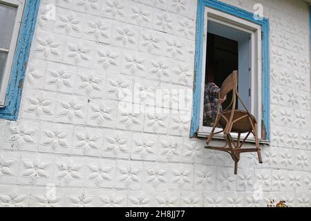 Ein Mann wirft einen alten Stuhl aus dem Fenster Stockfoto