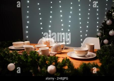 Weihnachtstisch, Teeparty, dekoriert mit Tannenzweigen. Es gibt Lichter im Hintergrund. Stockfoto