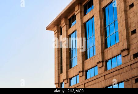 Blick auf das moderne Geschäftshaus mit keramischen Fassadenverkleidungen und großen massiven Glasfenstern. Einzelhandelsgebäude mit sandgefliesten Außenflächen vor blauem Himmel Stockfoto