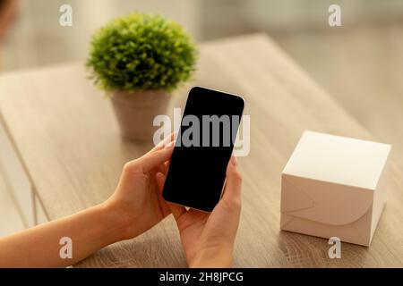 Weibliche Hände halten Smartphone mit schwarzem leeren Bildschirm für Mockup, Kopierplatz für Website oder App-Design Stockfoto