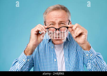 Reifer Mann, der mit einer Brille zuckt und die Kamera anschaut Stockfoto