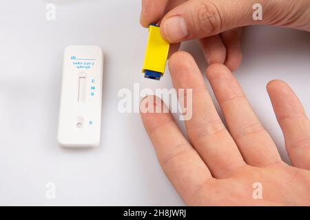 Isolierter Schuss von zwei einer Hand mit einer Lanzette, die eine Blutprobe vom Finger und einem leeren Rapid Express-Antigen Antobody Coronavirus covid-19 pandemic t entnahm Stockfoto