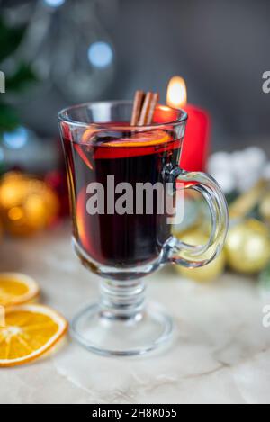 Köstlicher scharf würziger roter Glühwein mit Orangen- und Zimtgewürzen in der Nähe des Weihnachtsbaums mit Dekorationen und Bokeh-Girlanden Stockfoto