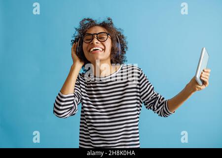 Fröhliche junge Frau, die Smartphone hält und Musik hört Stockfoto