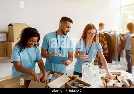 Junge Gruppe von multirassischen Freiwilligen, die in einem gemeinnützigen Spendenzentrum der Gemeinde arbeiten und gespendete Lebensmittel in Kartons sortieren Stockfoto