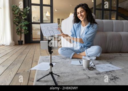 Schöne junge Frau zeigt Dokument auf Smartphone-Webcam, Teilnahme an Online-Business-Meeting zu Hause Stockfoto