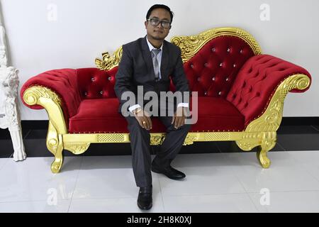 Porträt eines hübschen Mannes in formellem Anzug, der auf einem roten Sofa sitzt Stockfoto