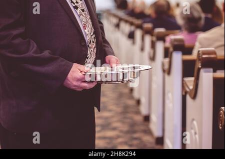 Mann, der in einer traditionellen amerikanischen Kirche an der Opferplatte vorbeikommt Stockfoto