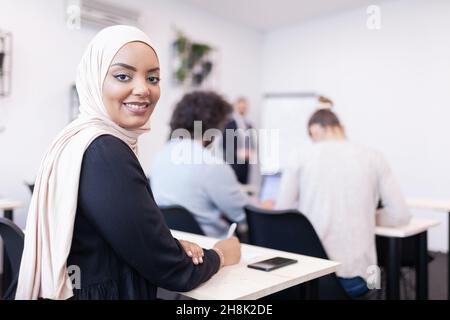 Multiethnische Studenten hören einem Dozenten in einem Klassenzimmer zu. Intelligente junge afroamerikanische Frau lächelt und posiert für die Kamera. Stockfoto