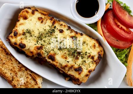 Lasagne auf weißem Teller mit Brot und Salat Stockfoto