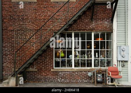 Backsteinfassade mit einem großen Fenster mit Lichtern und einem ausrangierten Stuhl, der an der Wand in Ipswich, Massachusetts, ruht Stockfoto