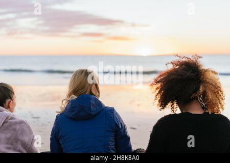 Frauen sitzen am Strand und blicken während des Sonnenuntergangs auf den Meereshorizont Stockfoto