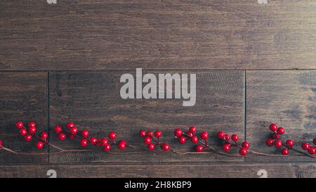 Rand von leuchtend roten Stechbeeren auf dunklem Holz mit Kopierfläche Stockfoto