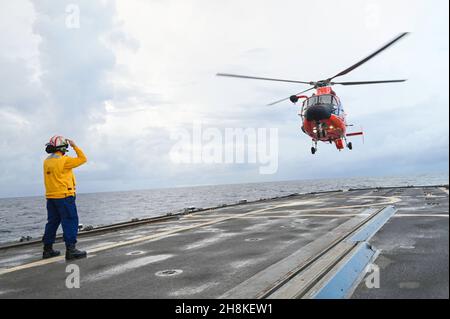 US Coast Guard LT. j.g. David Guerreiro führt den Piloten eines MH-65 Dolphin-Hubschraubers von der US Coast Guard Air Station Houston zur Landung auf dem Flugdeck des USCGC Thetis (WMEC 910) vor der Küste Nordkubas am 22. November 2021. Eine Flugabteilung mit einem Hubschrauber von der US-Küstenwache-Luftstation Houston schloss sich der Crew der Thetis an, bevor sie im US-6th-Flottenbereich eingesetzt werden. (USA Foto der Küstenwache von Petty Officer, Klasse 3rd, John Hightower) Stockfoto
