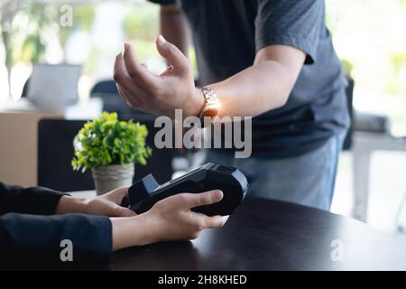 Moderner Mann, der eine Versicherung oder Hausrechnung per Smartwatch bezahlt. Zahlung über nfc-Technologie wird akzeptiert. Stockfoto