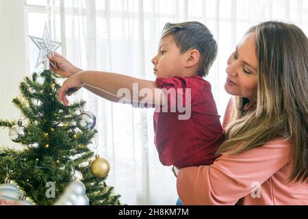 Mutter trägt ihren Sohn, um den Stern auf den weihnachtsbaum zu setzen Stockfoto