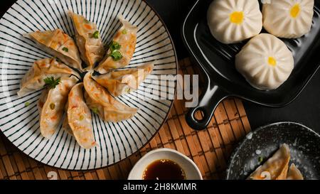Leckere gedämpfte chinesische Knödel oder japanische Gyoza-Knödel mit einem Teller Schweinebraten auf dem Tisch. Draufsicht. Stockfoto