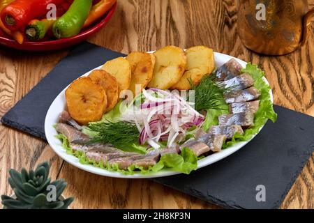 Marinierter Hering mit gebackenen Kartoffeln und Zwiebeln in Steingutplatte Stockfoto