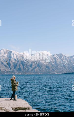 Frau mit Papiertüte steht auf dem Pier und füttert die Möwen Stockfoto