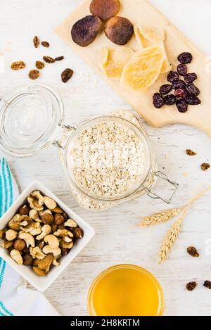 Draufsicht auf Rohzutaten für die hausgemachte Granola-Zubereitung - Hafer, Nüsse, Honig und getrocknete Früchte. Gesundes Essen. Stockfoto