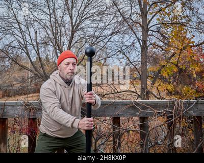 Älterer Mann (Ende der 60er Jahre) trainiert mit einer Stahlmace in seinem Hinterhof, Herbstlandschaft Stockfoto