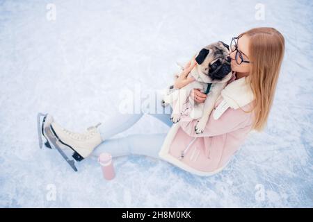 Junge Frau geht in den Wintersport auf Eislaufbahnen mit Mops Hund. Stockfoto