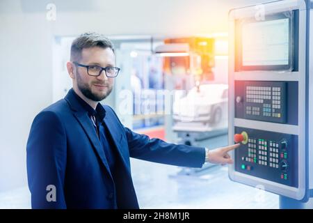 Industriearbeiter Mann in Gläsern, die CNC-Laser-Drehmaschine auf automatischem modernen Fabrikboden bedienen. Stockfoto