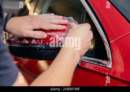 Meister Mann installiert Vinyl-Folie schützen Farbe Körper Seitenspiegel Auto. Stockfoto