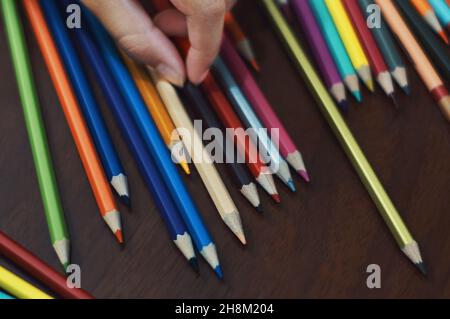 Eine Hand, die die Farbstifte auf dem Tisch auswählt Stockfoto