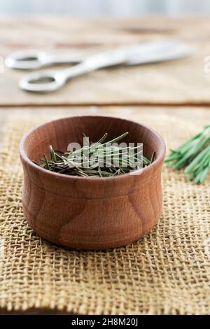 Rosmarin in einer Holzschüssel mit einer Schere auf dem Tisch trocknen. Rustikaler Stil. Das trockene Gewürz wird zu Fleisch, Salaten, Suppen oder Getränken hinzugefügt. Zutat für die bo Stockfoto