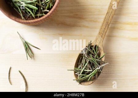 Trocknen Sie Rosmarin in einer Holzschüssel mit einem Löffel und kleinen Zweige auf einem Holztisch. Rustikaler Stil. Das Gewürz wird zu Fleisch, Salaten, Suppen oder Getränken hinzugefügt. Ingr Stockfoto