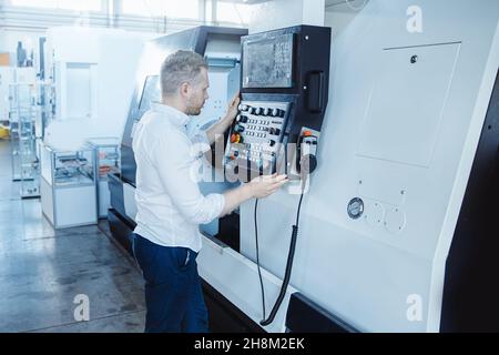 Junger männlicher Ingenieur, der CNC-Maschinen in der Eisenmetallfabrik betreibt Stockfoto