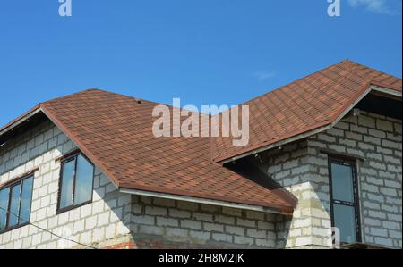 Ein asphaltierter Dachboden als oberer Dachbereich eines neuen Hauses, das aus Betonblöcken gebaut wurde. Eine Nahaufnahme eines braunen Asphaltschingeldachs w Stockfoto