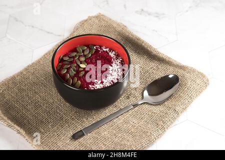 Eine Schüssel mit Apfel- und Rote Beete-Smoothies mit Kürbiskernen und Kokosnusssplittern auf einer Stoffserviette. Heller Hintergrund Stockfoto