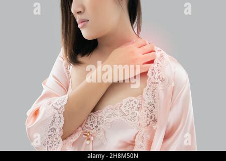 Asiatische Frau juckt Hals und Schulter auf einem grauen Hintergrund Stockfoto