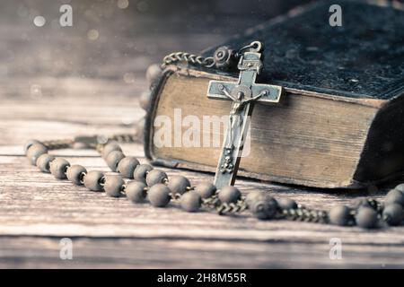 Detail Studioaufnahme einer sehr alten, alten Heiligen Bibel mit vielen Ornamenten auf dem Cover und gelben Seiten und einem alten Rosenkranz auf einem alten Holzschreibtisch Stockfoto