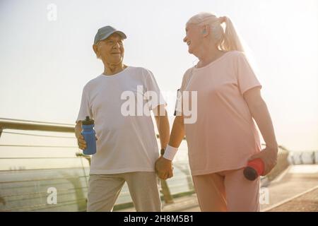 Sportlich reife Frau und Mann gehen bei Sonnenuntergang mit Händen entlang der Brücke Stockfoto
