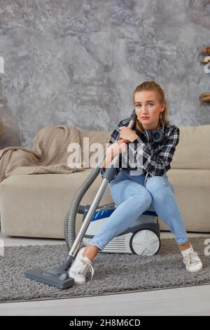 Junge Frau mit Reinigungsausrüstung bereit, Haus zu reinigen, sitzt auf der Couch. Müdigkeit Stockfoto