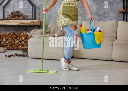 Reinigungsservice. Eimer mit Schwämmen, Chemieflaschen und Wischstock. Zugeschnittenes Bild einer Frau mit einem Wischmopp im Wohnzimmer Stockfoto