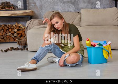 Frau Hausfrau fühlen sich müde sitzen auf dem Boden im Wohnzimmer nach der Reinigung zu Hause. Stockfoto